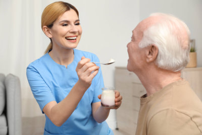 nurse feeding elderly men with yogurt indoors. assisting senior people