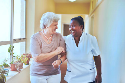 portrait of smiling home caregiver and senior women walking together through a corridor. healthcare worker taking care of elderly woman.